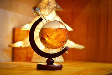 Whisky in Glass Bottle Globe with Glowing Christmas Tree Background