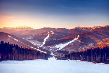 Ski resort in beautiful sunset light. View from the top: ski tracks, pine tree forest and mountains...
