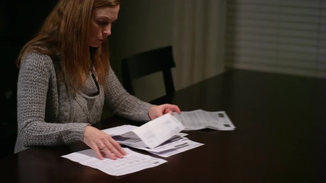 A woman looking over bills at the table, looking stressed