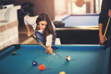 Young beautiful young woman aiming to take the snooker shot whil