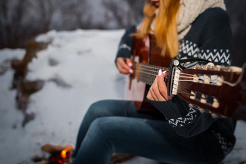 Girl playing guitar in the mountains near the fire burning