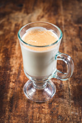 latte in a tall glass beaker on wooden table