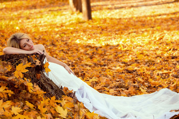 Beautiful sexy young girl lying on the ground strewn with autumn leaves, leaning on a picturesque stump of a tree.Long beautiful curls.Photos in style of high key.Fashionable toning.Creative color.