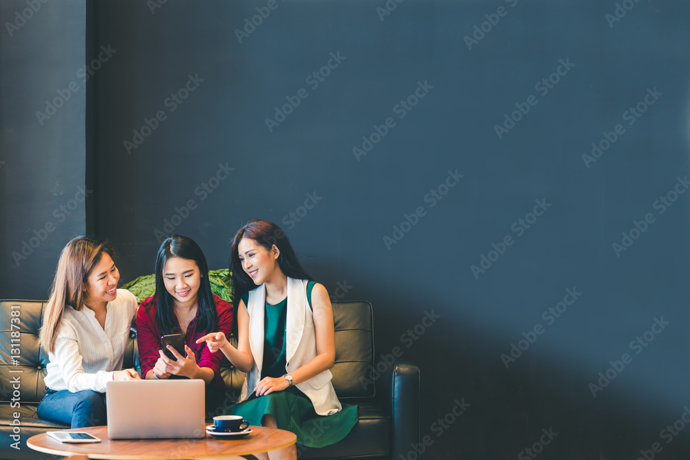 Wall mural three beautiful asian girls using smartphone and laptop, chatting on sofa at cafe with copy space, m