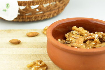 Wallnuts and almonds in earthenware pot on wooden chopping board with basket in frame