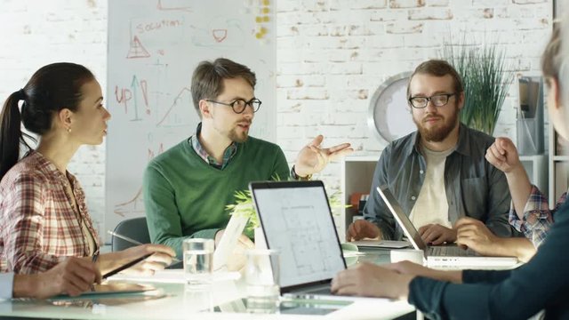 Group of Young Creative People Have Strategic Planning Session. They are Sitting at Big Glass Table with Open Laptops in their Bright and Modern Loft Office. Shot on RED EPIC (uhd). 