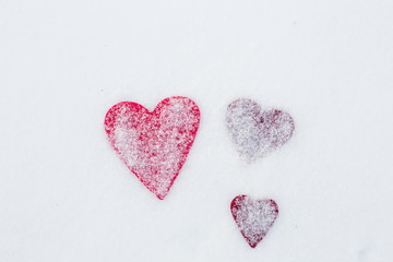 Three red felt heart shapes in snow, Valentine's Day. Copy space for text. Snowflakes on hearts. Valentines day, love concept. White background