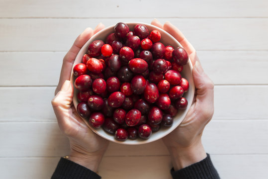 Cranberries in a bowl, held in a womans hands.