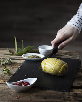 Hasselback potatoes: woman's hand cutting a potato on wooden tab
