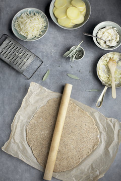 Pie dough and ingredients for a potato galette. Photographed on a greay background from top view.