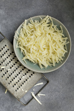 Ceramic Bowl of Shredded Cheese with Vintage Cheese Grater, Photographed on grey background from top view.