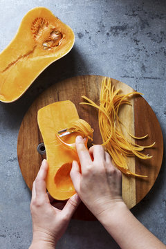 Female hands making butternut squash noodles with a vegetable peeler.Top view.