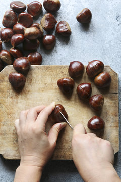 Female hands scoring chestnuts before roasting.Top view