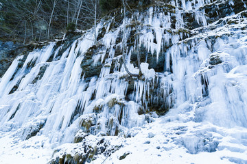 Fototapeta na wymiar Frozen icicles on rocky wall at the mountain, closeup with selec
