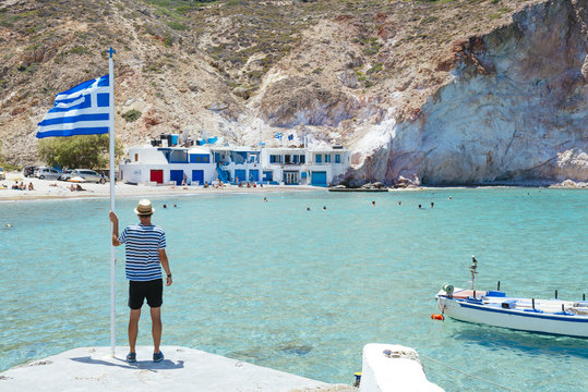 Greece, Milos, Firopotamos Beach, man looking at sea, holding onto Greek flag