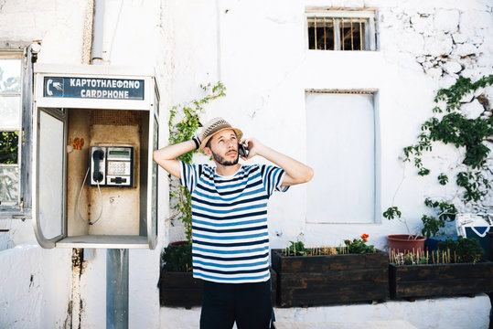 Greece, Milos, Klima, Man talking on cell phone, leaning against old telephone booth
