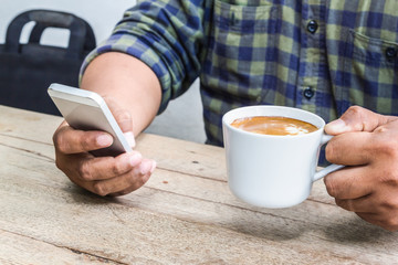 man 's hand hold smartphone and coffee cup