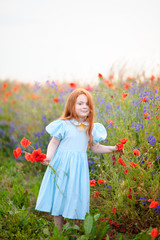 Naklejka premium cute child redhead posing near blooming poppy field with red wil