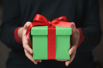 female teen hands show green paper gift box with red bow