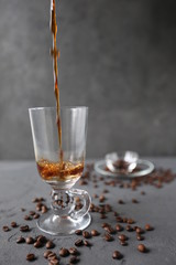 hot coffee in the tall glass with coffee beans on the grey stone table.