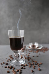 hot coffee in the tall glass with coffee beans on the grey stone table.