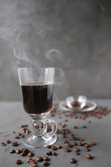 hot coffee in the tall glass with coffee beans on the grey stone table.