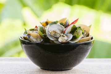Cooked mussels with green leaves and red pepper in a black plate