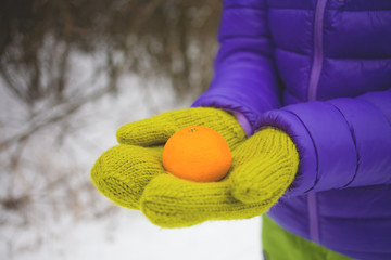 Female hands in mittens holding a tangerine. © zhukovvvlad