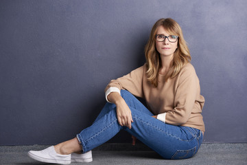 Shot of a mature woman with pretty face sitting by the wall while wearing casual clothing and smiling.