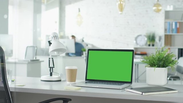 Creative Office Shot of Green Screened Laptop Standing on the Table with Nobody Working on It. In the Background Man Comes in and Sits at His Workplace Starts Working. Shot on RED EPIC (uhd).