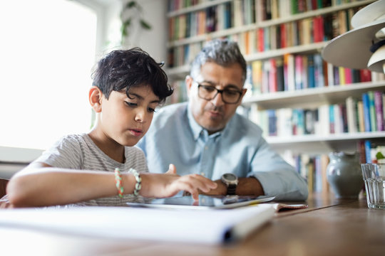 Father assisting son in using digital tablet while studying at brightly lit home