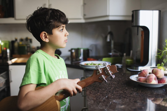 Thoughtful boy holding guitar while standing at kitchen counter