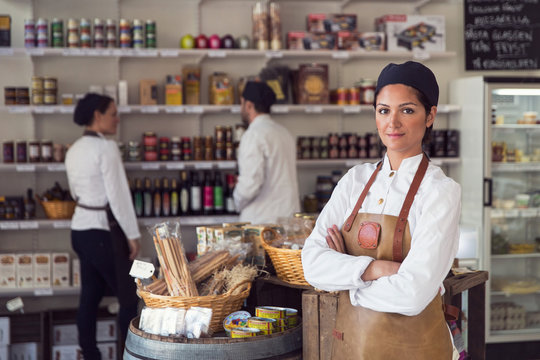 Portrait of confident owner standing arms crossed while colleagues working in grocery store