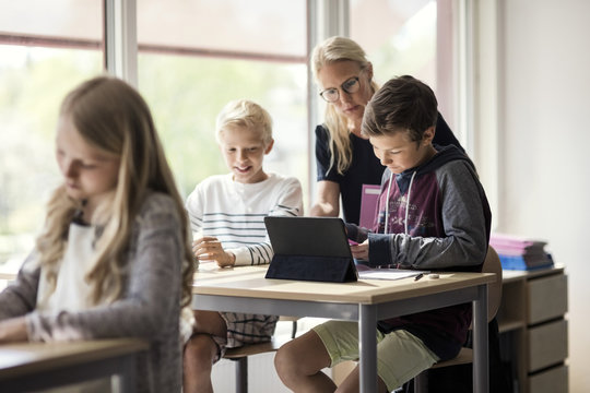 Teacher assisting children in e-learning from digital tablet