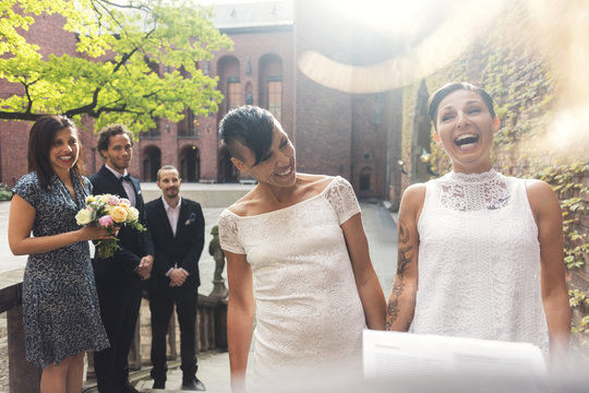 Cheerful lesbian couple and guest laughing during ceremony