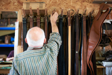 Male worker in leather workshop, hanging leather belts on rack, rear view