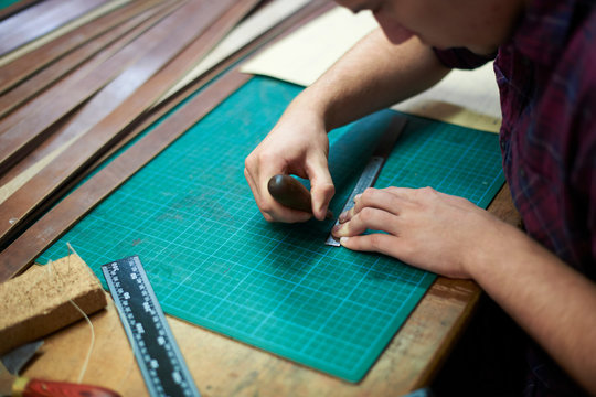 Male worker in leather workshop, measuring leather, using bradle