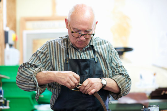 Male worker in leather workshop, polishing belt buckle