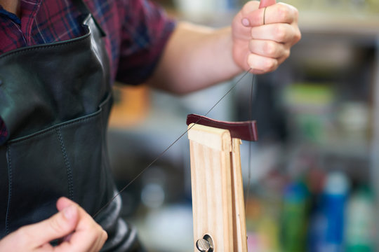 Male worker in leather workshop, sewing up watch strap, mid section, close-up
