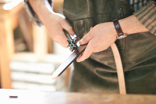 Male worker in leather workshop, punching holes in leather belt, mid section, close-up