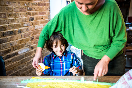 Mother helping son spread glue on crepe paper to make pinata
