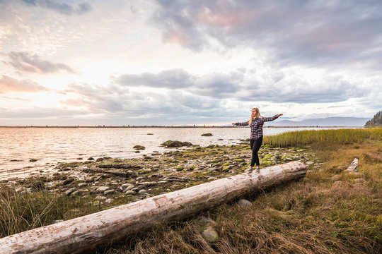 Woman balancing on tree trunk at Wreck Beach, Vancouver, Canada