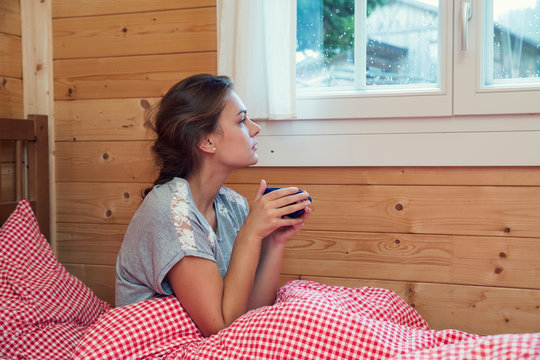 Young woman looking through window from log cabin bed, Tyrol, Austria
