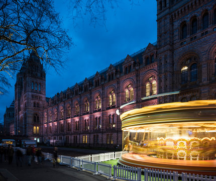 Illuminated spinning carousel by Natural History Museum at dusk, London, UK