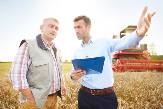Farmer and businessman in wheat field holding clipboard looking away