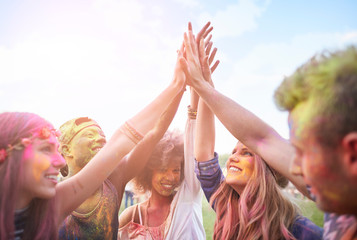Group of friends at festival, covered in colourful powder paint, joining hands
