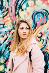 Half length portrait of young beautiful caucasian blonde hair woman leaning on a colorful wall, overlooking smilng - carefree, serene, thoughtless concept