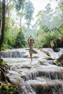Woman standing on one leg, in tree pose, in Kuang Si waterfall, Luang Prabang, Laos