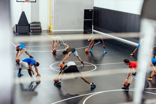 Male trainer and basketball players warming up stretching forward on court