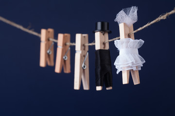 Bride and groom clothespin toys, clothesline. Abstract woman in white dress and man character with black suit hat. Love concept photo. Macro view, shallow depth of field, blue background